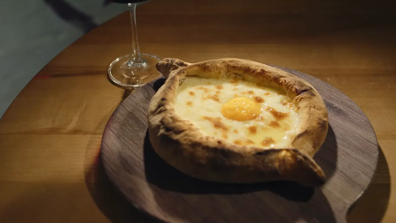 Baked Ajaruli khachapuri with melted cheese and a sunny egg in the center on a wooden board next to a wine glass