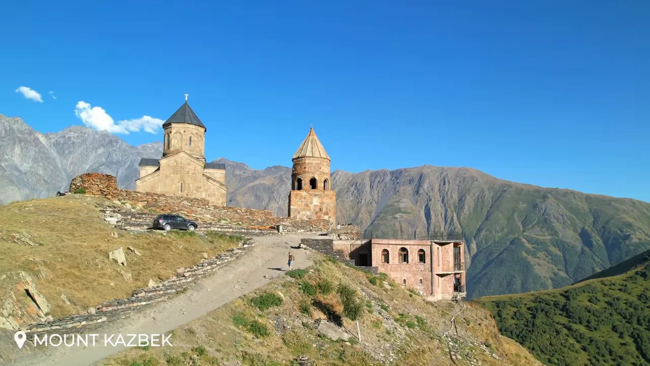 Gergeti Trinity Church on a hilltop with a clear blue sky and layered mountain slopes behind