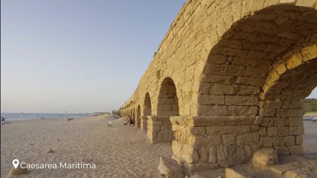Ancient stone aqueduct arches extending along a sandy beach